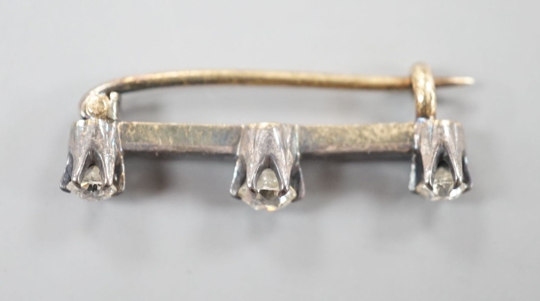 An early 20th century yellow metal and three stone diamond set bar brooch, 26mm, gross 2.1 grams.